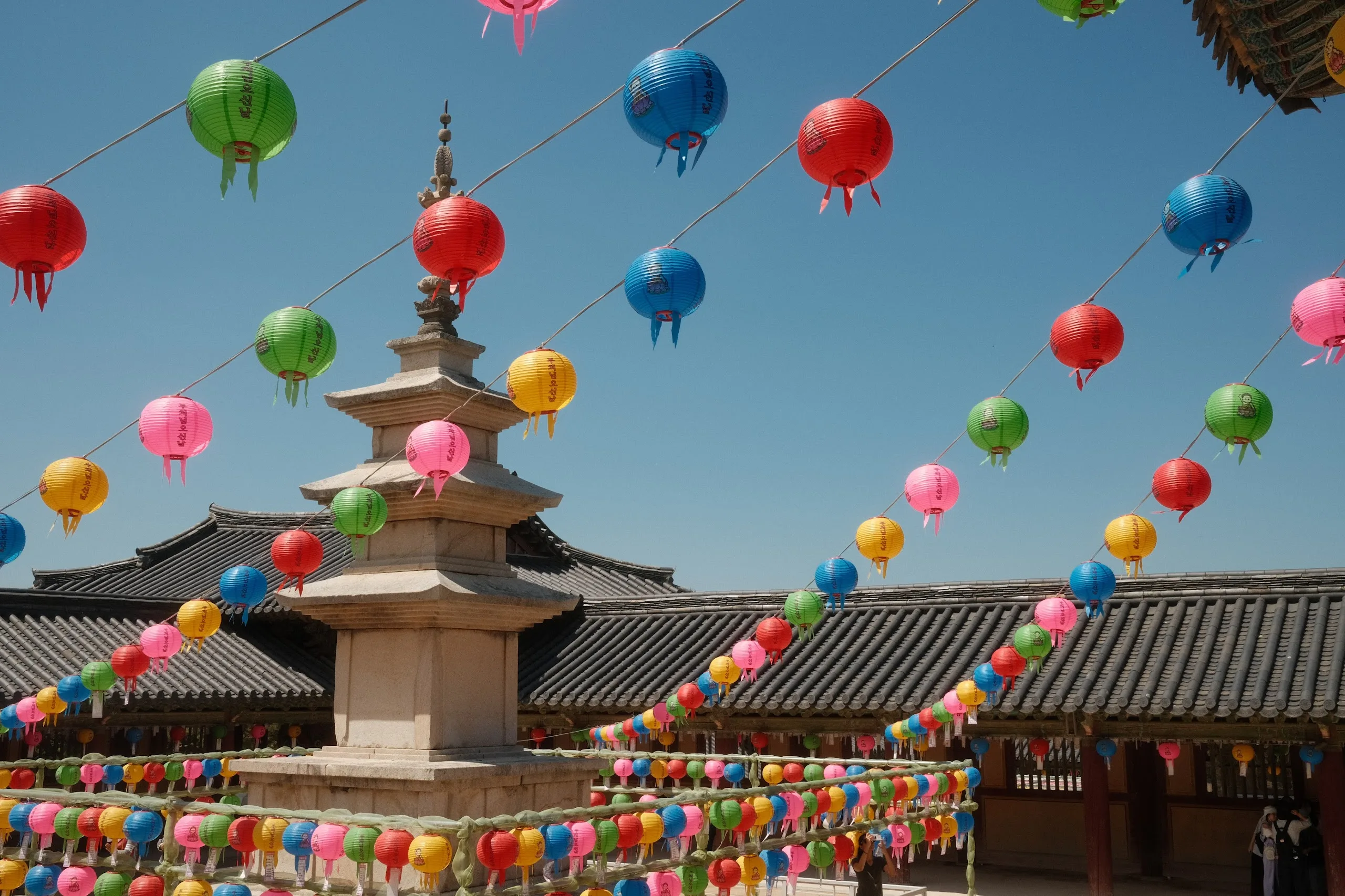 A stone pagoda in a temple courtyard framed by colourful lotus lanterns under a blue sky