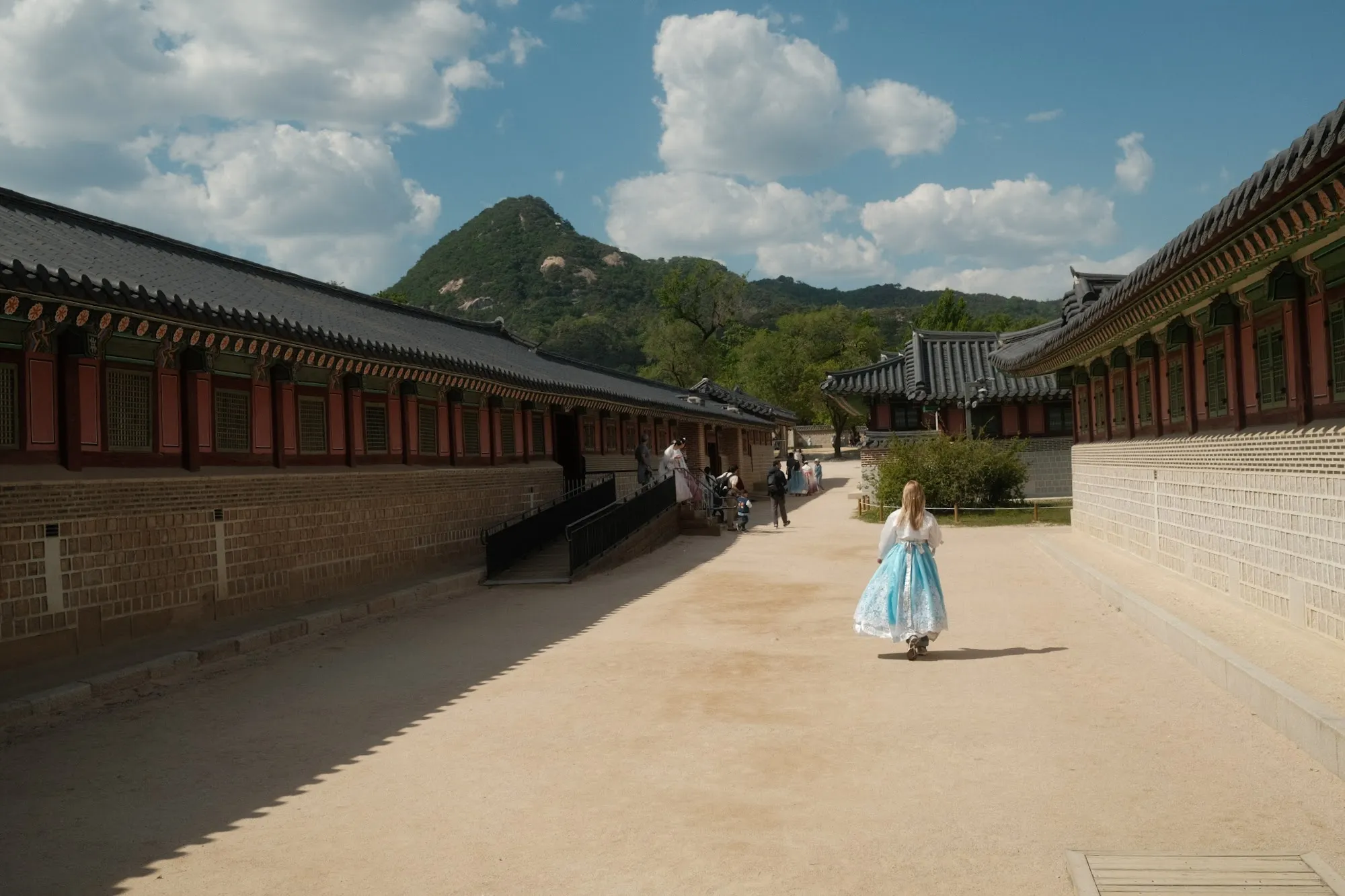 A figure in hanbok along a long palace wall