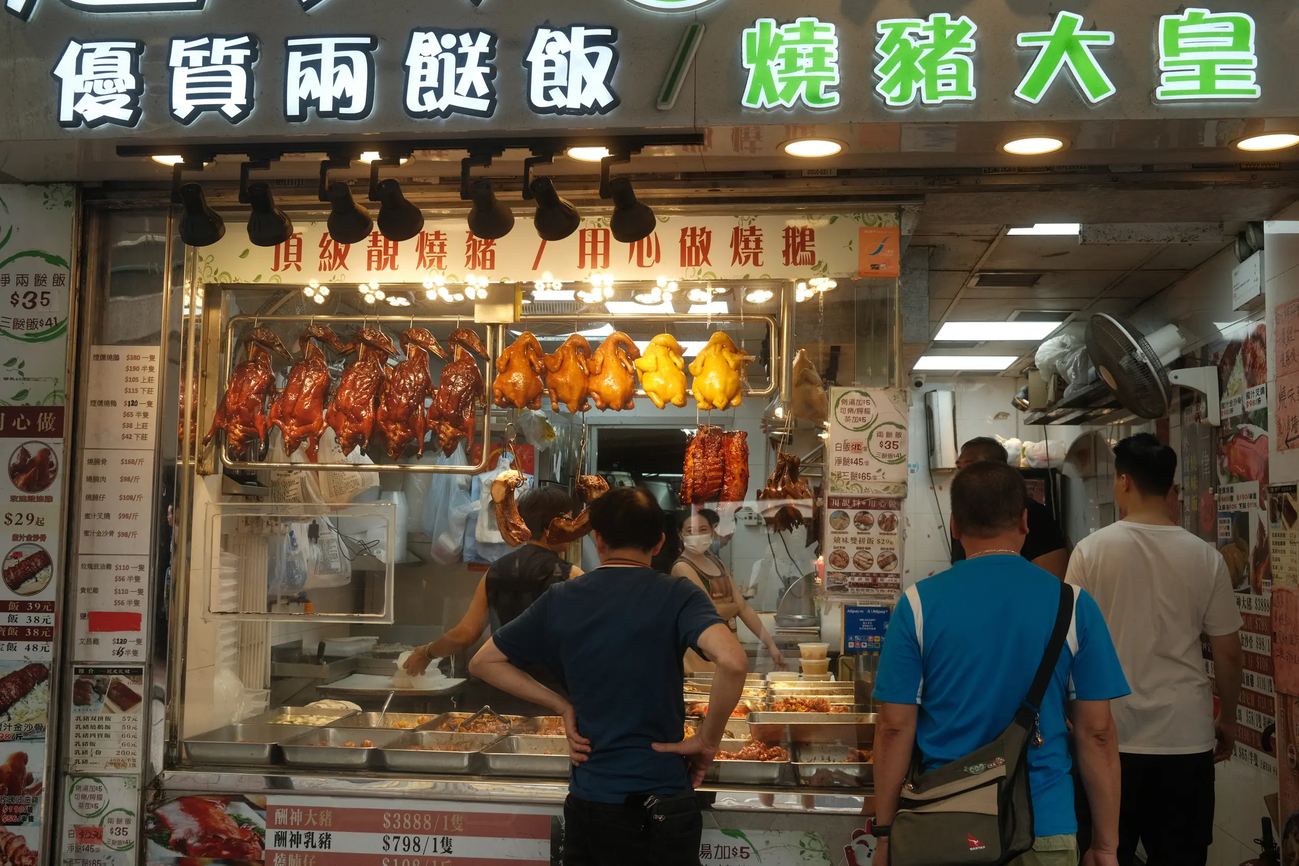 Roast geese hanging in a shop window with green neon signage