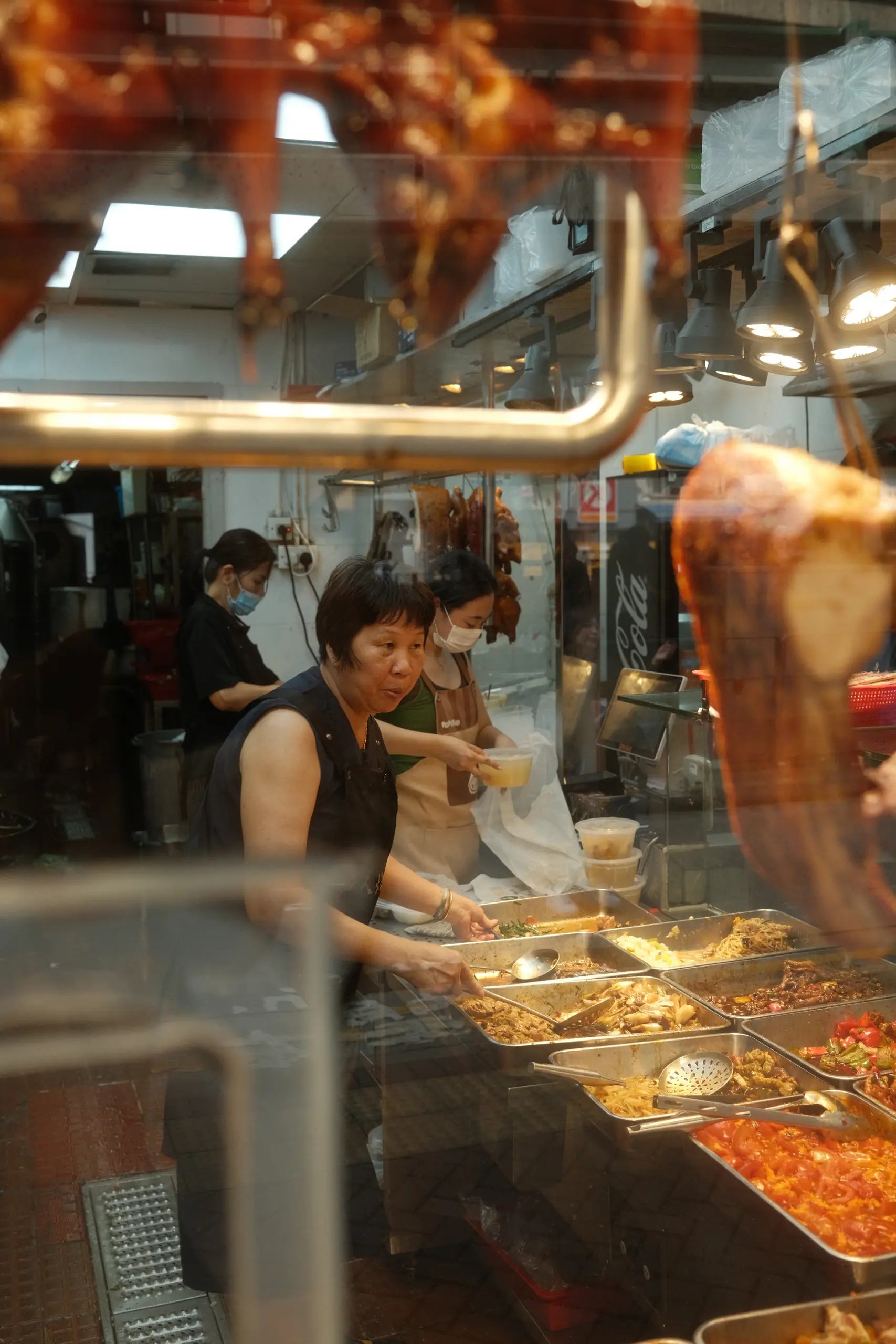A cook chopping roast meat behind a glass counter