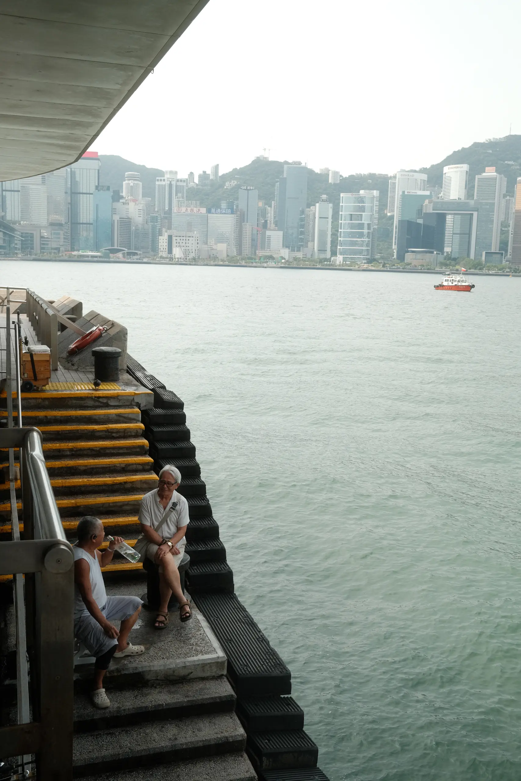 People sitting on steps at the harbour edge with the skyline across the water