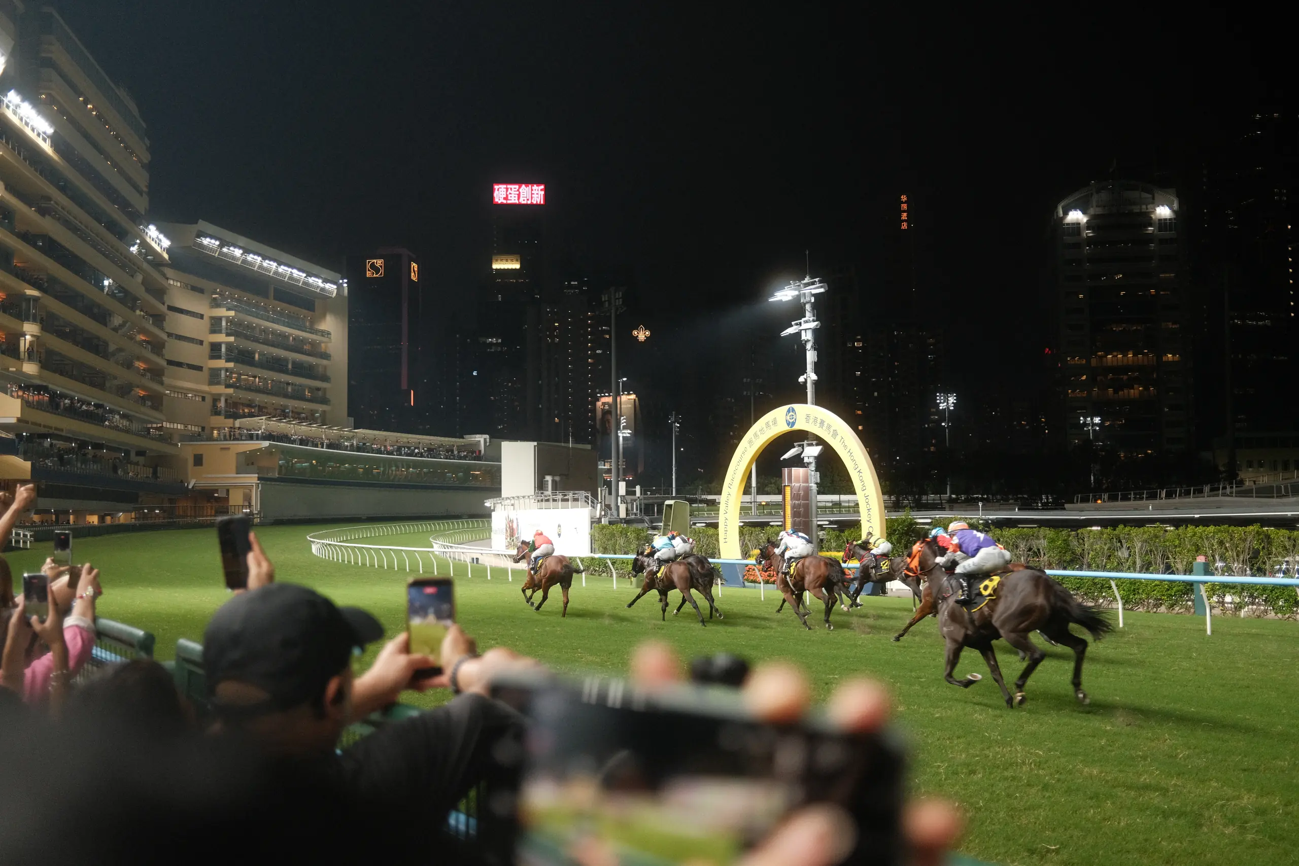 Horses crossing the finish line at Happy Valley under floodlights