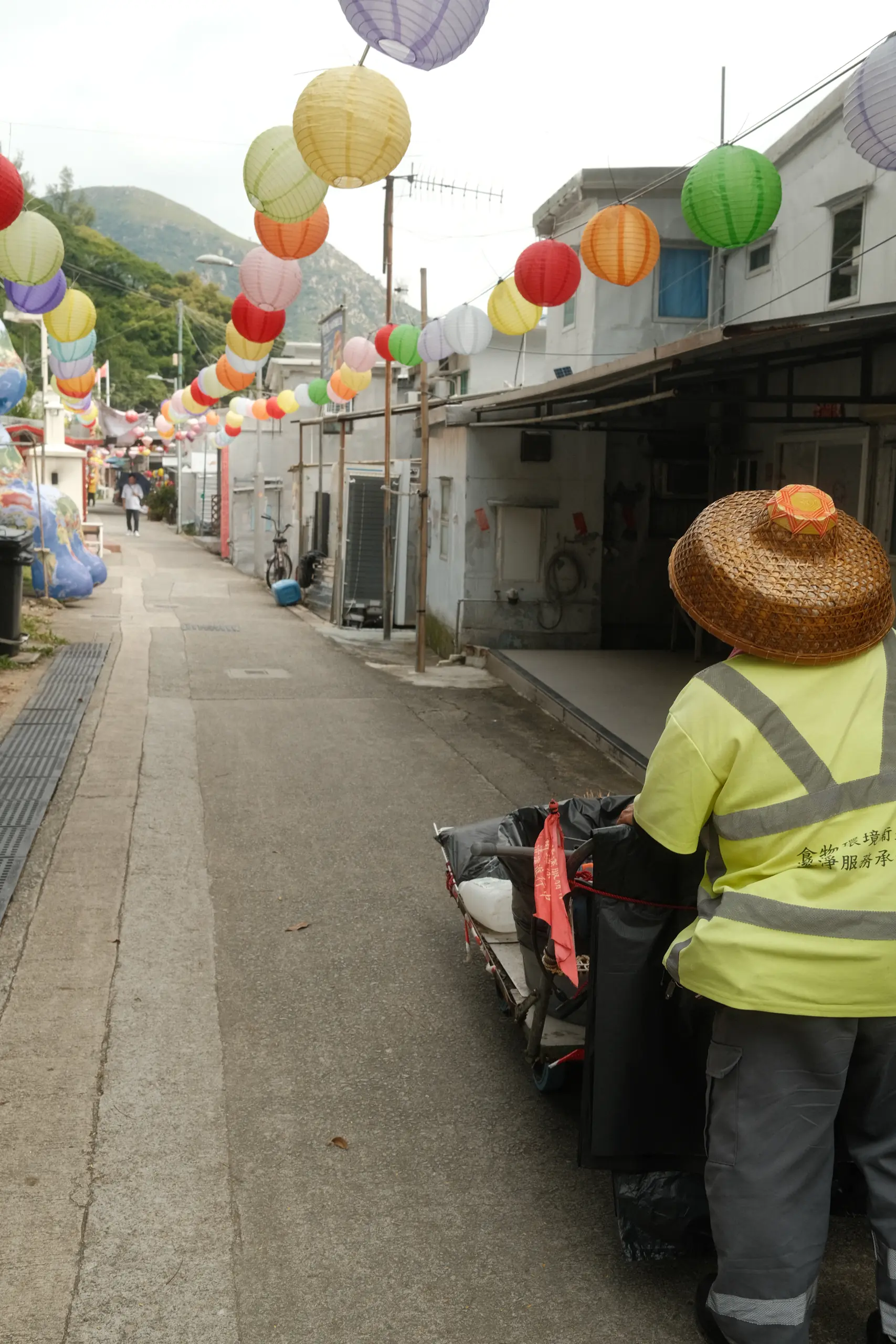 A worker in a straw hat under paper lanterns in a Tai O lane
