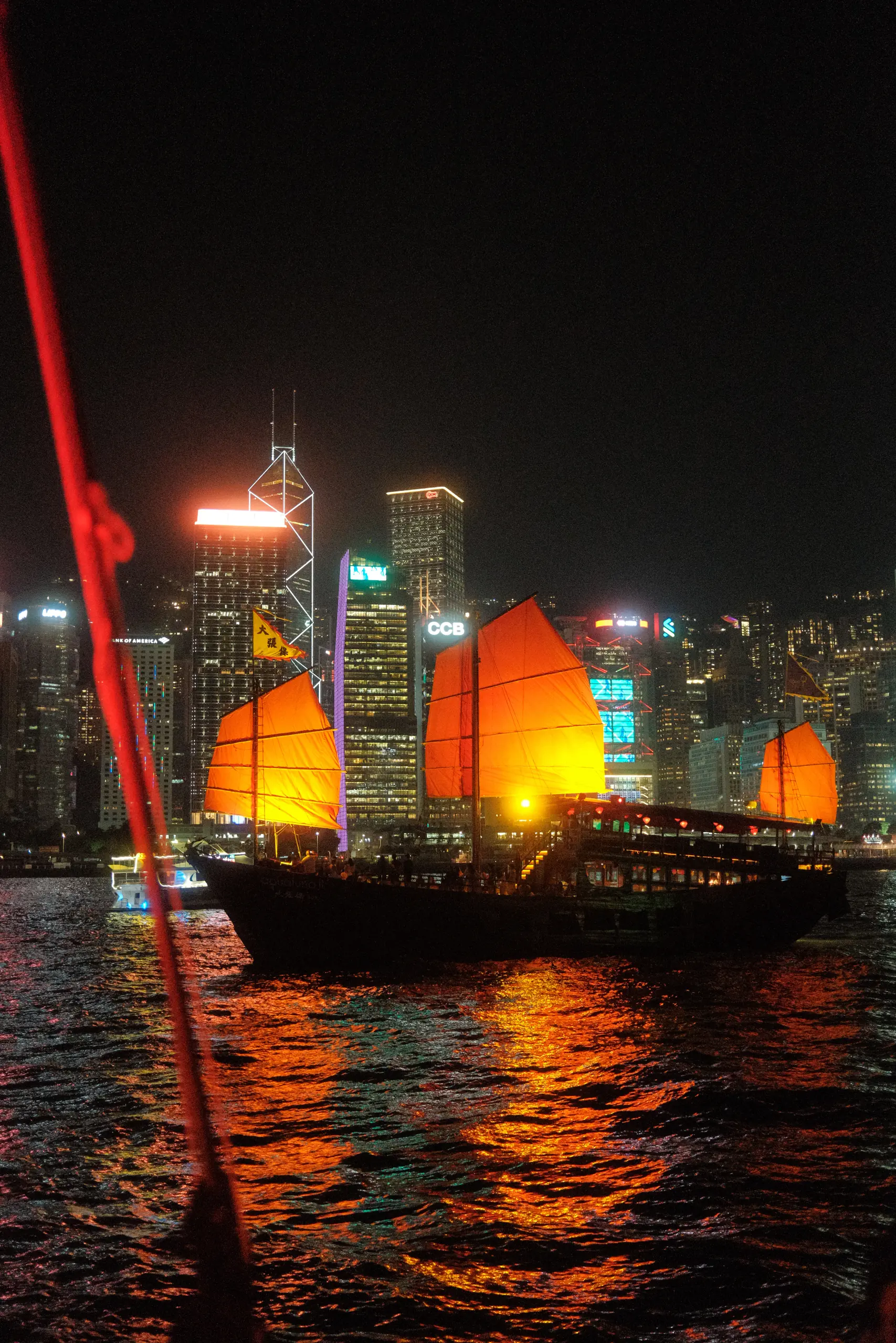 A red-sailed junk crossing the harbour at night