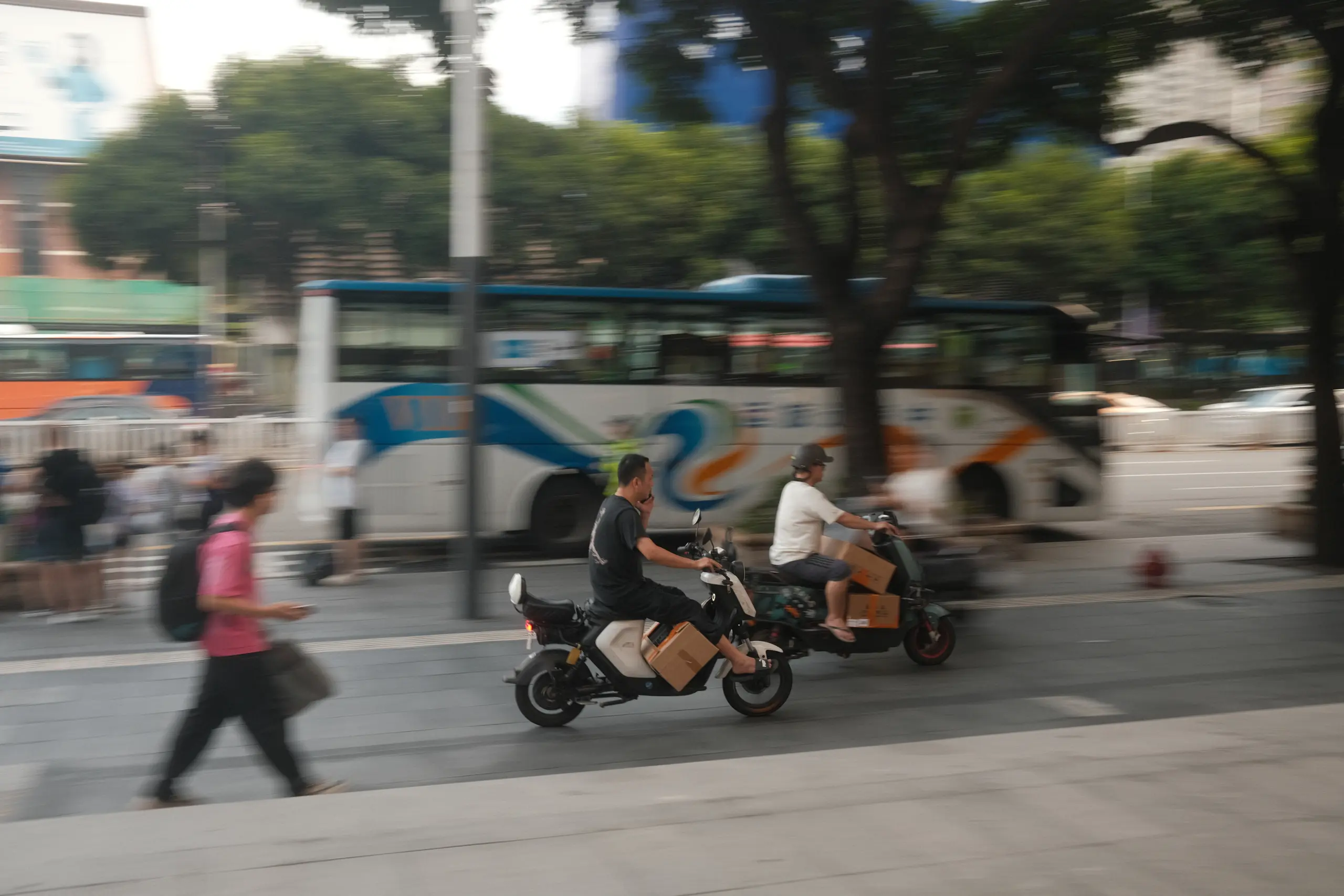 A couple on an electric scooter passing a bus stop