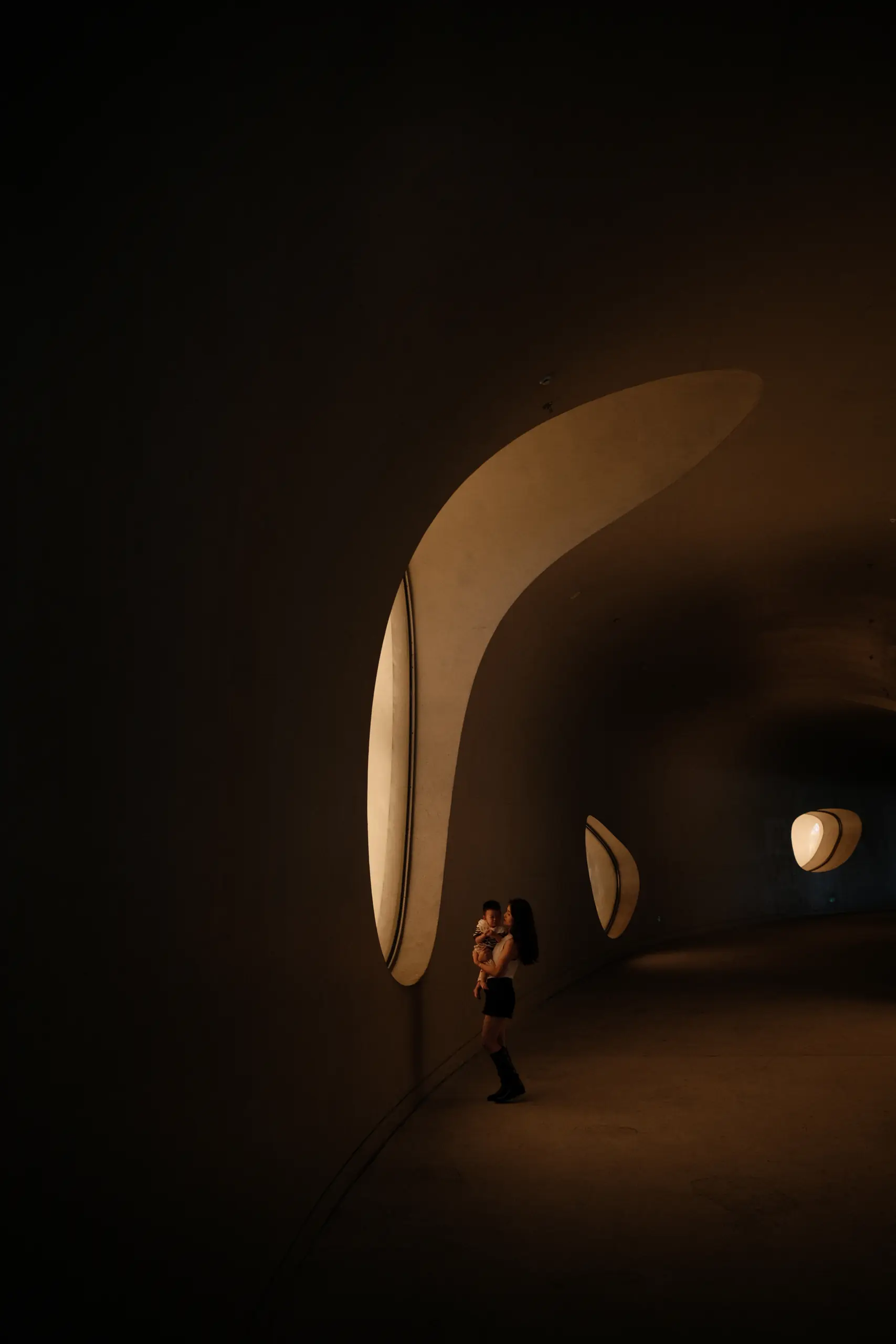 A visitor in a dark gallery lit by curved openings