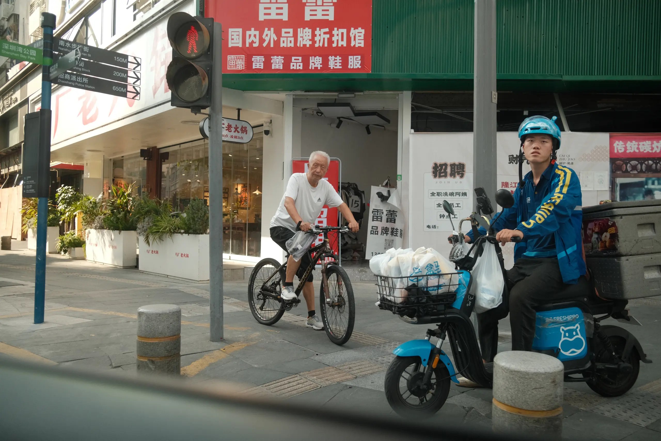 Two people on electric scooters waiting at a crossing