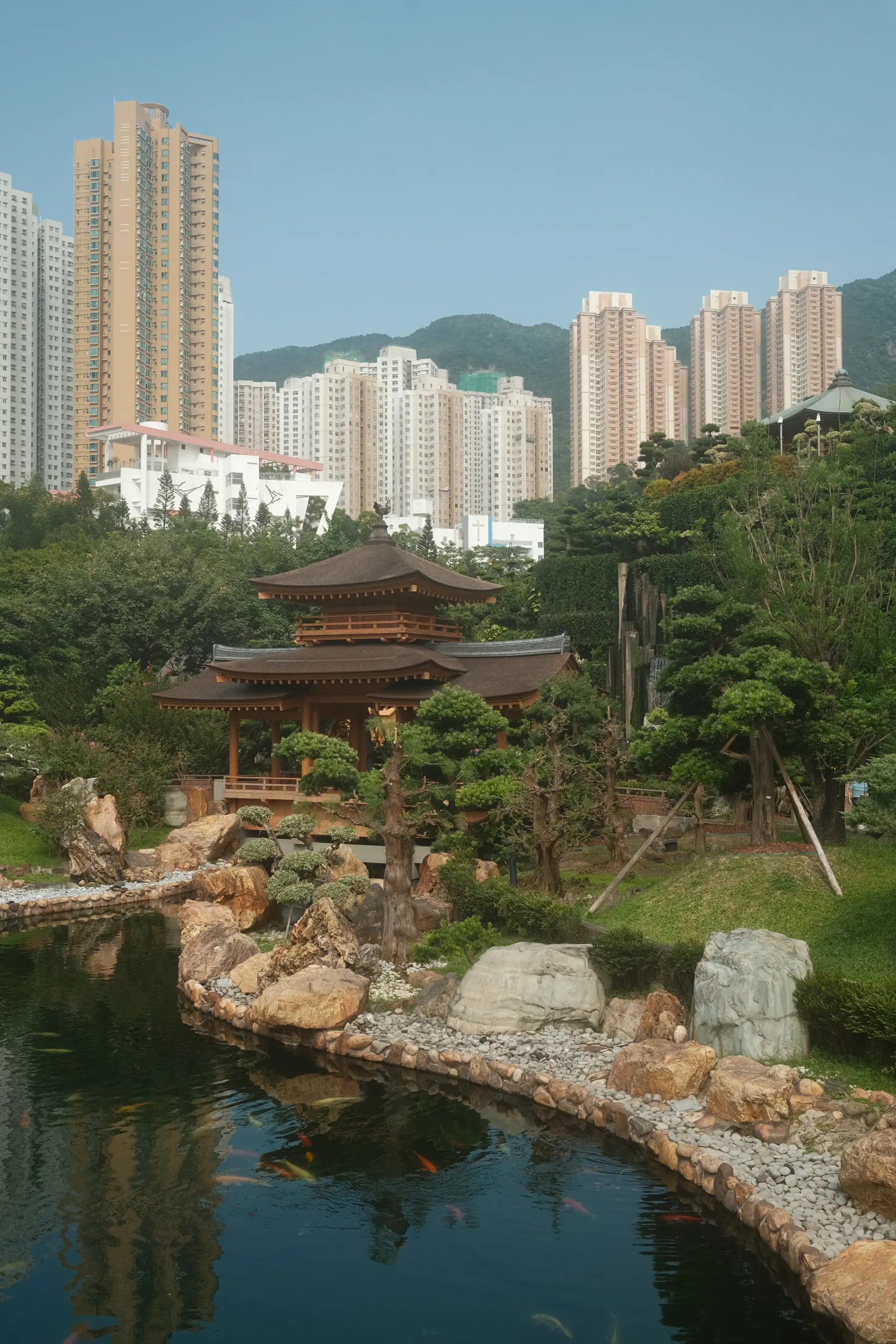 A wooden pavilion by a pond in Nan Lian Garden with towers behind