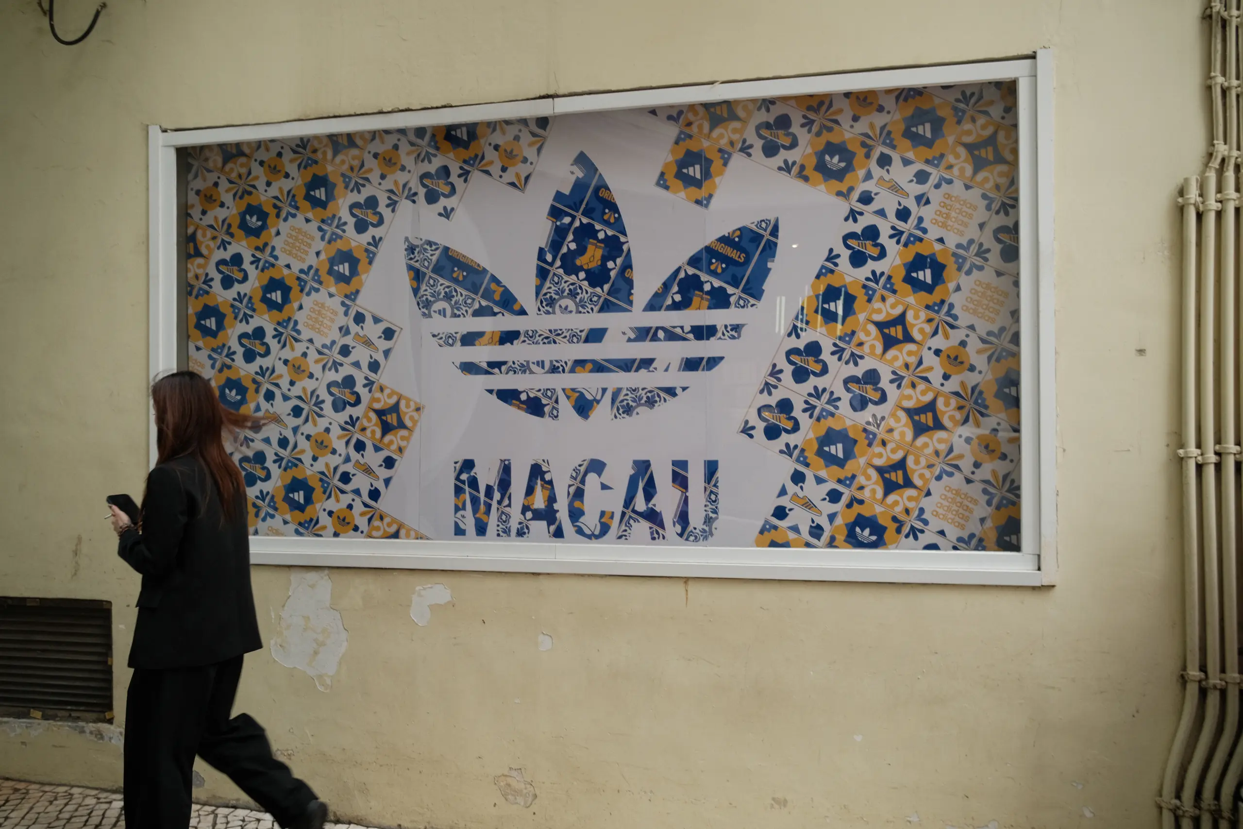 A tiled mural reading Macau with a passer-by
