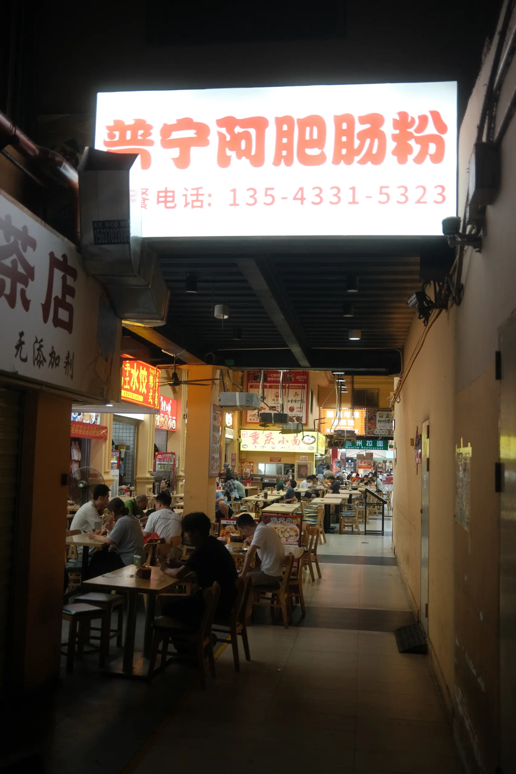 An illuminated sign above a noodle shop in a food court