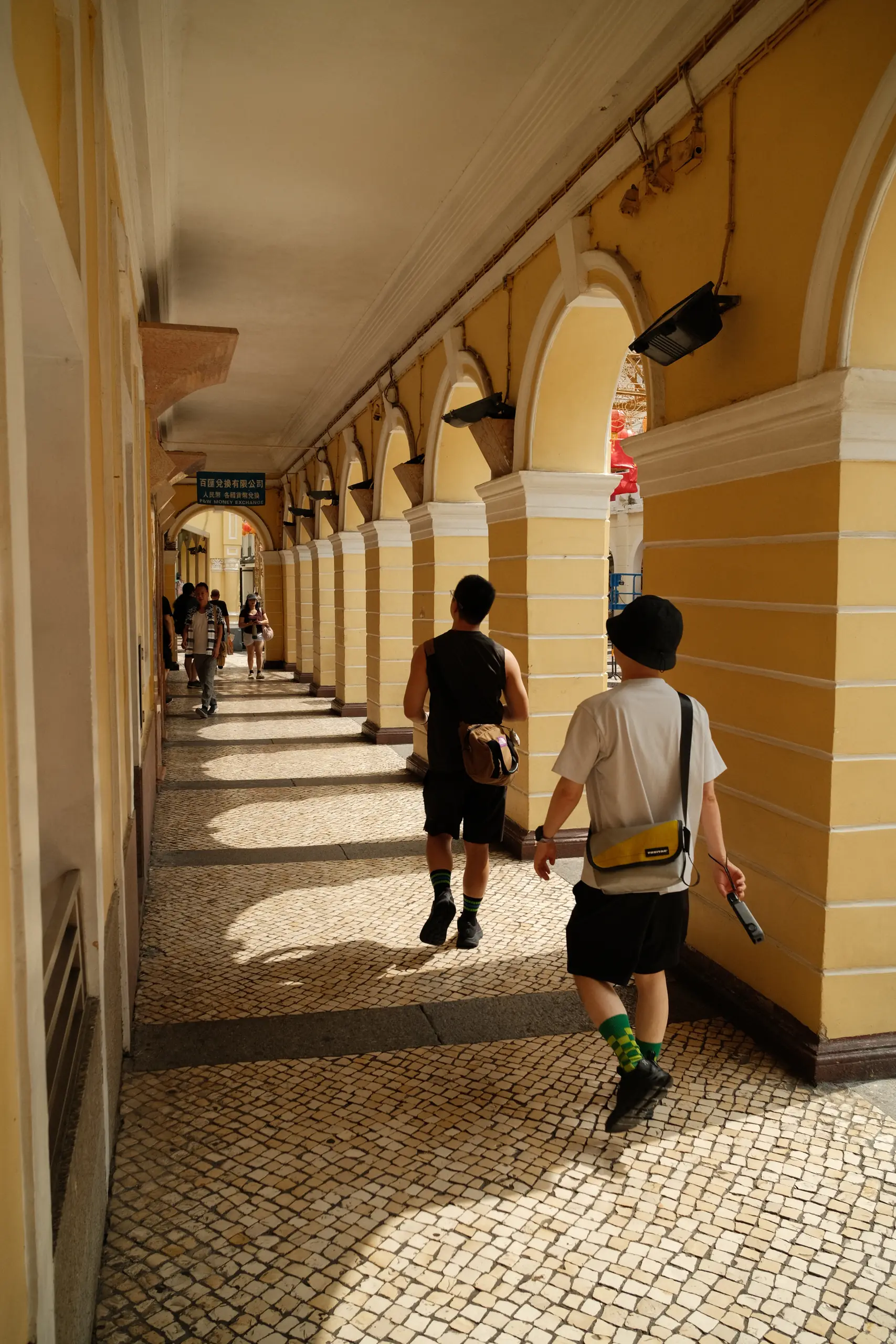A yellow arcade with people walking through the shade