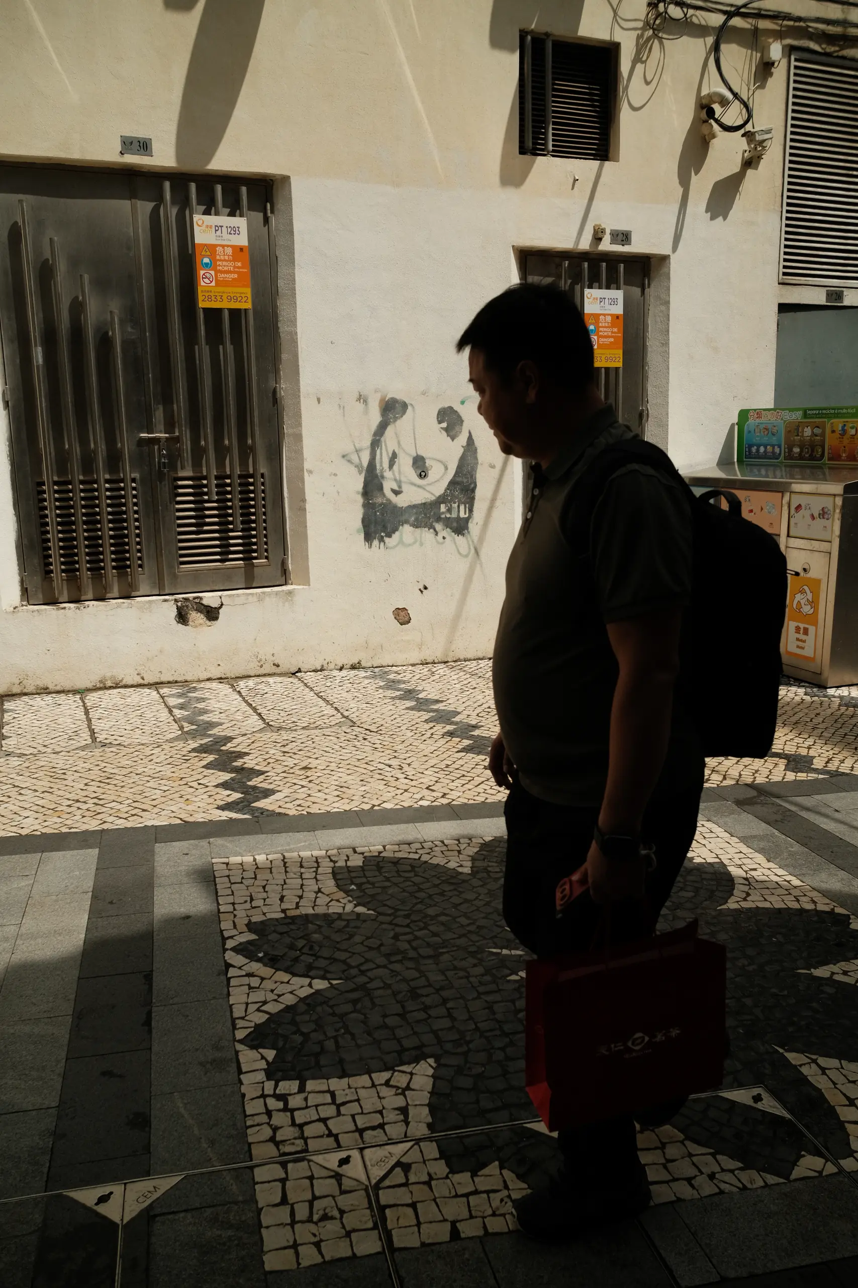 A man standing on Portuguese pavement next to a panda graffiti