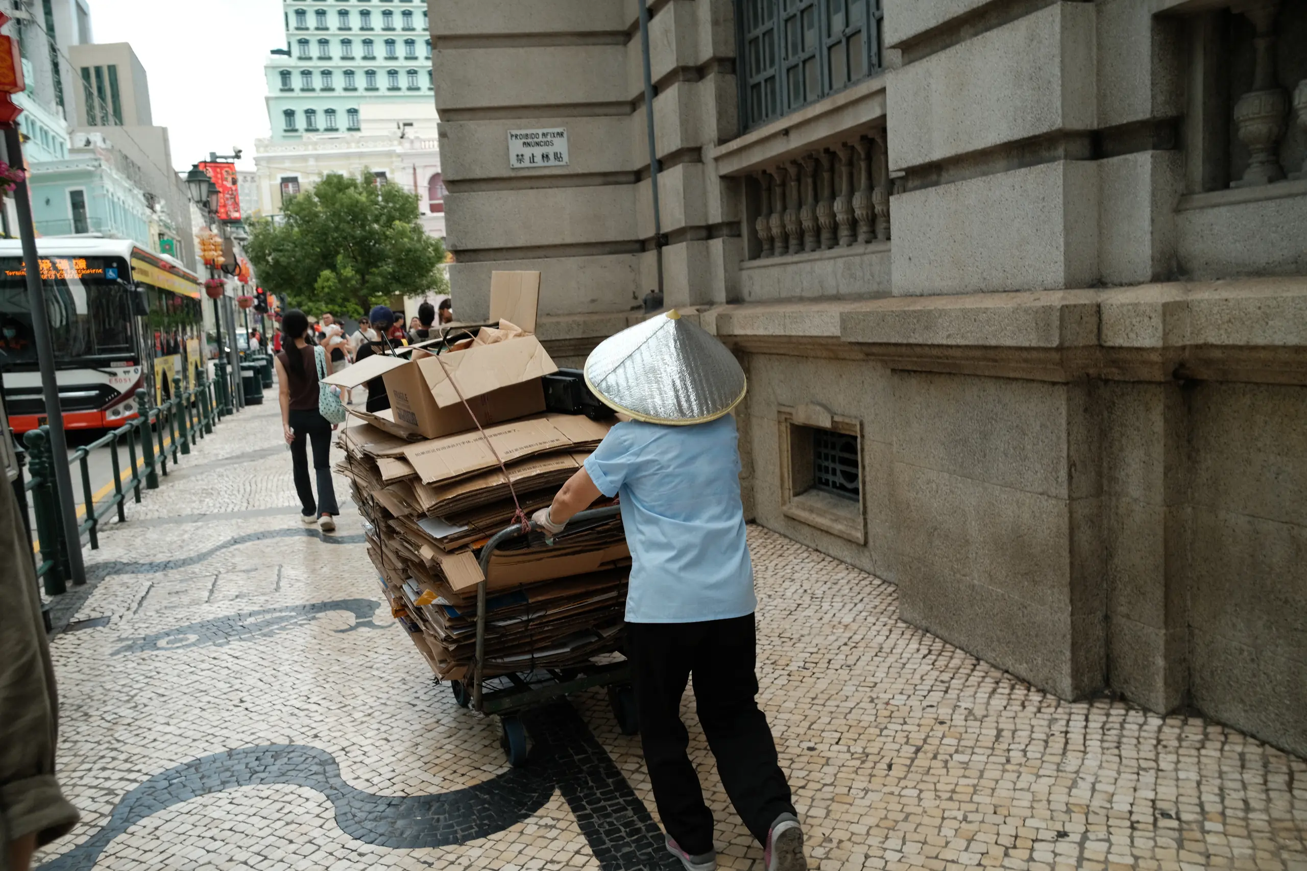 A woman pushing a cart stacked with cardboard along a cobbled street