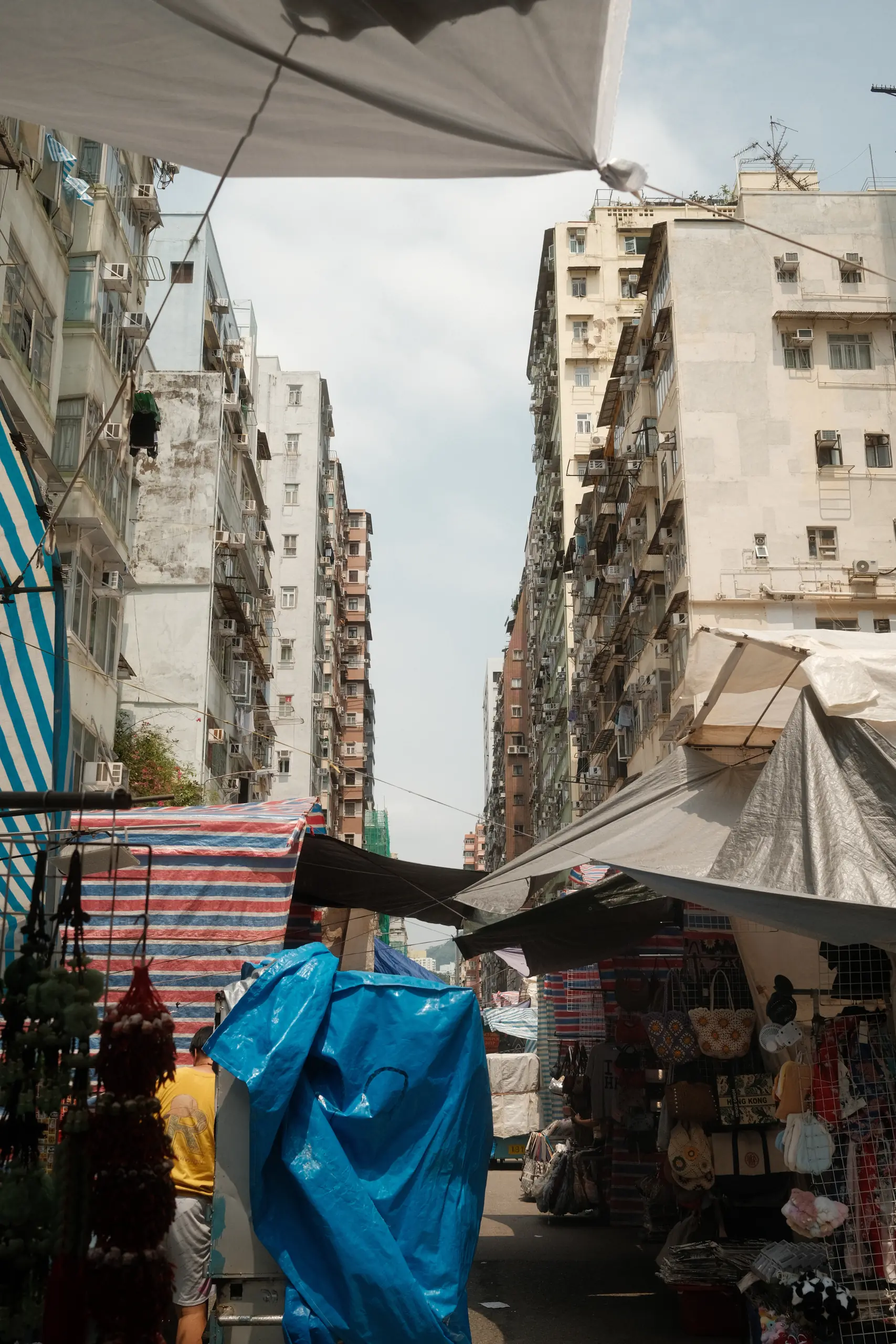 A street market under blue tarpaulins between tenement blocks